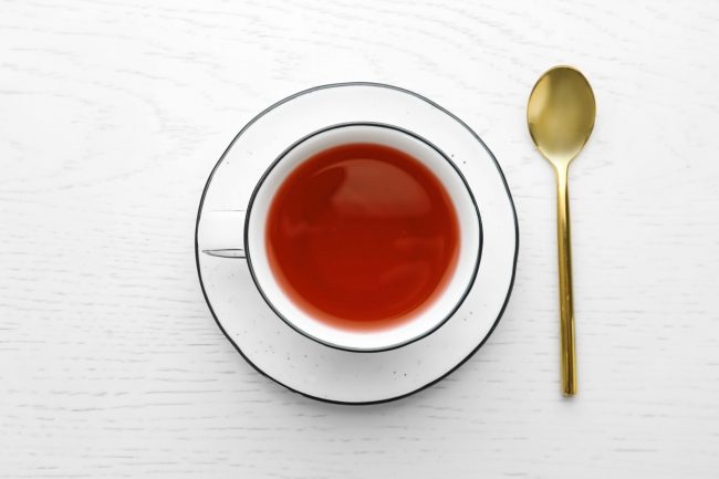 Cup of hibiscus tea with saucer and spoon on white wooden background, flat lay